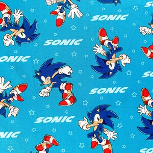 Op de afbeelding: Blauw en wit stof met een herhalend patroon van Sonic the Hedgehog die rent en het woord "SONIC" in een blauw en wit lettertype.