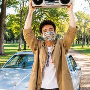May include: A silver portable cassette player with two large speakers held overhead. The device features a central cassette deck, various control knobs, and a handle. It is a classic boombox design with a metallic finish and black speaker grilles.