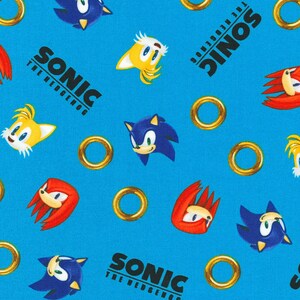 Op de afbeelding: Een blauwe achtergrond met herhalende afbeeldingen van Sonic the Hedgehog-personages, waaronder Sonic, Tails, Knuckles en gouden ringen. De tekst "Sonic The Hedgehog" wordt herhaald in het hele patroon.