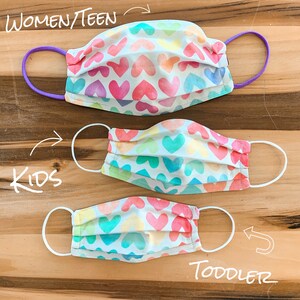 May include: Three face masks with a rainbow heart pattern. The masks are in different sizes, labelled "Women/Teen", "Kids", and "Toddler".