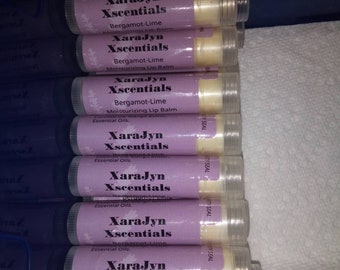 May include: A stack of XaraJyn Xscentials lip balms. The lip balm tubes have a light purple label with the text "Bergamot-Lime Moisturizing Lip Balm" and "Essential Oils." The tubes are clear, showing the balm inside. The net weight is 0.375 oz / 5.5 ml.
