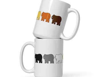 Puede incluir: Dos tazas de cerámica blanca apiladas una encima de la otra. La taza superior tiene una línea de cinco osos de diferentes colores: amarillo, naranja, marrón, gris y blanco. La taza inferior tiene una línea de cuatro osos de diferentes colores: negro, gris, blanco y amarillo.