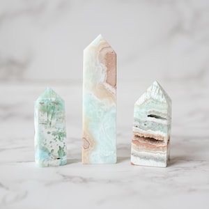 May include: Three green, white, and brown crystal towers of varying sizes on a white marble surface.