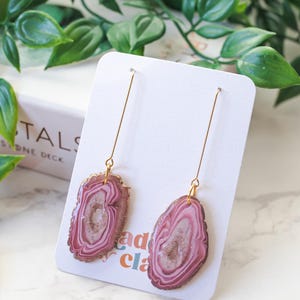 May include: A pair of dangle earrings with pink and white agate-like resin and gold-colored wire.