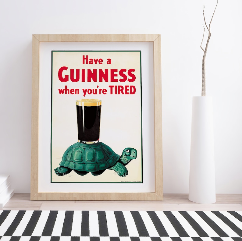 Op de afbeelding: Een vintage Guinness reclameposter met een groene schildpad die een glas Guinness draagt. De poster luidt "Have a GUINNESS when you're TIRED."