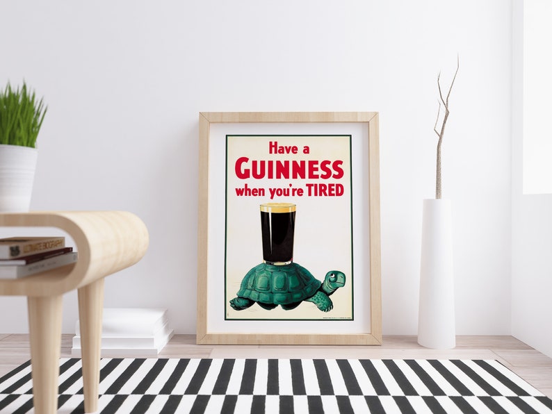 Op de afbeelding: Een vintage Guinness-reclame met een groene schildpad die een glas Guinness draagt met de tekst "Have a GUINNESS when you're TIRED".