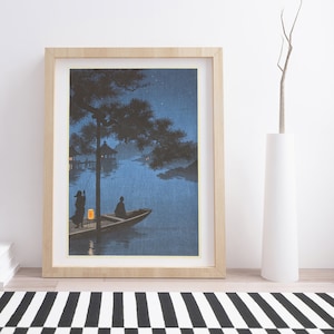 May include: A framed print of a Japanese woodblock print depicting two figures in a boat on a lake at night. The scene is illuminated by a lantern in the boat and stars in the sky. The print is framed in a light wood frame.