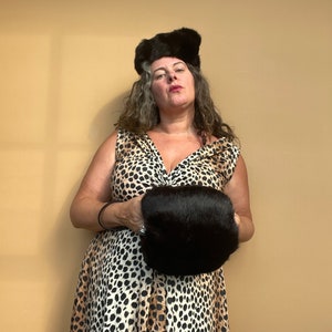 May include: A woman wearing a black and white animal print dress with a black fur hat and a black fur clutch.