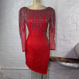 May include: A red beaded dress with long sleeves and a fringe hem. The dress is made of a sheer fabric and is covered in silver beads.