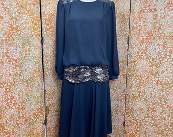 May include: A black long-sleeved dress with a lace overlay at the shoulders and waist. The dress has a flowing skirt and is on a mannequin.