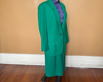 May include: A green blazer and skirt suit. The blazer has a single button closure and a pocket on each side. The skirt is knee-length.