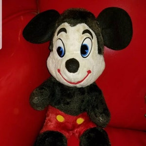 K&ouml;nnte beinhalten: Ein Vintage-Pl&uuml;schtier Mickey Mouse mit schwarzem Fell, roten Shorts mit gelben Kn&ouml;pfen und gelben Schuhen. Das Spielzeug hat ein wei&szlig;es Gesicht mit schwarzen Augen und einer schwarzen Nase.