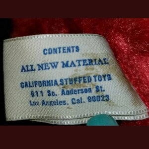 K&ouml;nnte beinhalten: Ein wei&szlig;es Etikett mit blauem Text, auf dem steht "CONTENTS ALL NEW MATERIAL CALIFORNIA STUFFED TOYS 611 So. Anderson St. Los Angeles. Cal. 90023".