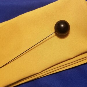 May include: A black ball on a thin black stick, placed on top of a folded yellow napkin.