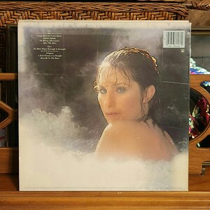 May include: Album cover featuring a woman in a bathtub, with the title and song list visible. The woman is looking over her shoulder. The album is in a protective sleeve. The background is dark with a white, foamy substance.