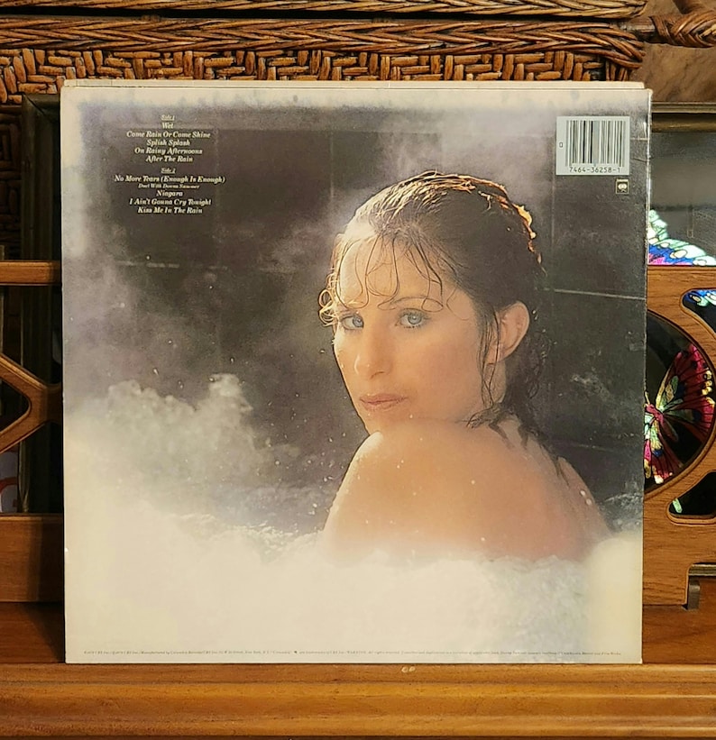 May include: Album cover featuring a woman in a bathtub, with the title and song list visible. The woman is looking over her shoulder. The album is in a protective sleeve. The background is dark with a white, foamy substance.