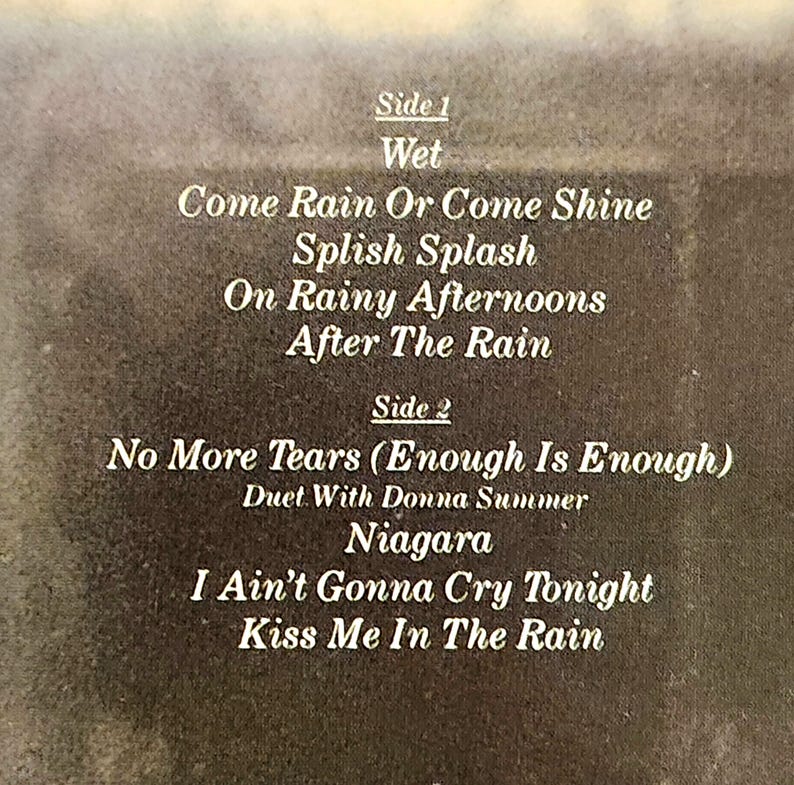 May include: A close-up of a vintage album cover with song titles in white text. The album is divided into Side 1 and Side 2, with song titles like "Come Rain Or Come Shine" and "No More Tears". The background is a faded brown.