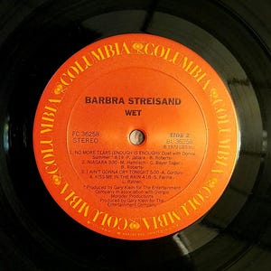 May include: A vintage vinyl record by Barbra Streisand, titled "WET." The orange and black record features the Columbia Records logo and song titles, including "No More Tears" and "Kiss Me in the Rain." The record is a stereo recording.