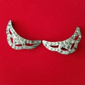 May include: A pair of silver crescent moon shaped earrings with clear rhinestones.