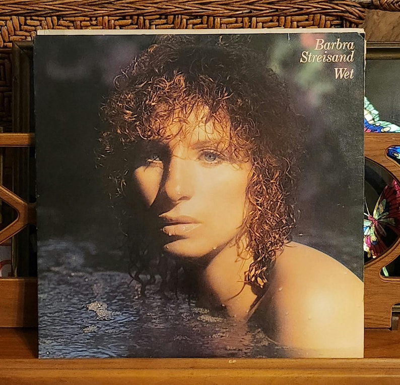May include: Vintage vinyl record album cover featuring Barbra Streisand. The album cover has a dark background with Streisand's face and shoulders emerging from water. The album title "Wet" is visible.