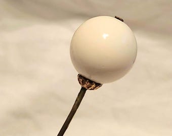 May include: A white ceramic ball on a gold-toned metal pin. The ball is smooth and round.