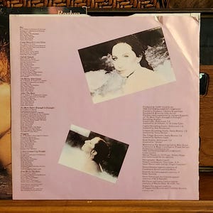 May include: The back cover of a vinyl record album. The album cover is light pink with two inset photos of a woman. Text on the cover includes song titles and production credits. The album is titled "Barbra".