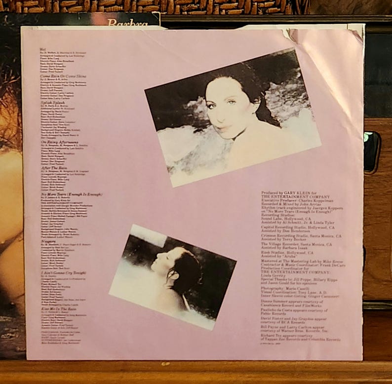 May include: The back cover of a vinyl record album. The album cover is light pink with two inset photos of a woman. Text on the cover includes song titles and production credits. The album is titled "Barbra".