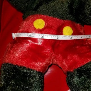 K&ouml;nnte beinhalten: Ein rotes und schwarzes Pl&uuml;sch-Mickey-Mouse-Spielzeug mit gelben Kn&ouml;pfen. Das Spielzeug wird mit einem Ma&szlig;band gemessen und zeigt, dass es 4 Zoll breit ist.