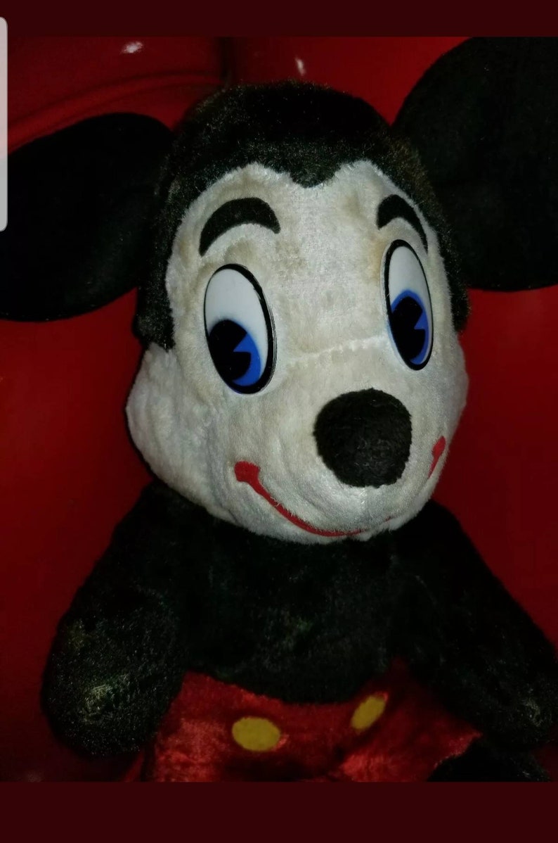 K&ouml;nnte beinhalten: Ein Vintage-Pl&uuml;schtier Mickey Mouse mit schwarzem Fell, wei&szlig;em Gesicht und roten Shorts mit gelben Kn&ouml;pfen. Das Spielzeug hat gro&szlig;e blaue Augen und eine schwarze Nase.