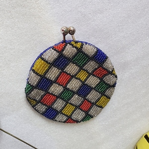 May include: A small, round beaded purse with a checkered pattern in shades of blue, red, green, yellow, and white. The purse has a silver clasp.