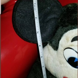 K&ouml;nnte beinhalten: Ein schwarzes und wei&szlig;es Pl&uuml;sch-Mickey-Mouse-Spielzeug mit gro&szlig;en schwarzen Ohren. Das Spielzeug wird mit einem Ma&szlig;band gemessen und zeigt, dass es etwa 15 cm gro&szlig; ist.