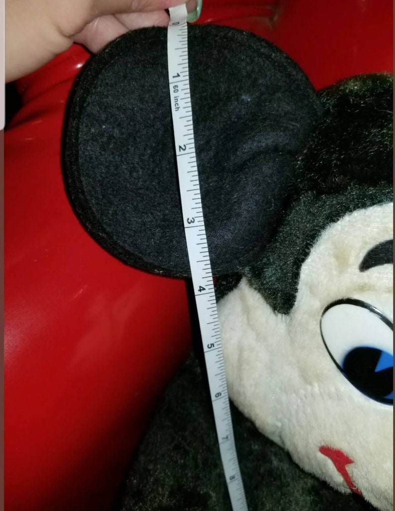 K&ouml;nnte beinhalten: Ein schwarzes und wei&szlig;es Pl&uuml;sch-Mickey-Mouse-Spielzeug mit gro&szlig;en schwarzen Ohren. Das Spielzeug wird mit einem Ma&szlig;band gemessen und zeigt, dass es etwa 15 cm gro&szlig; ist.