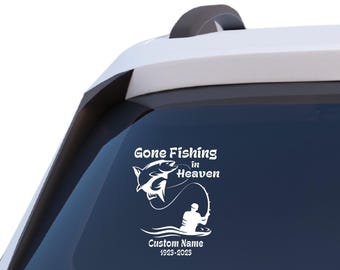 Peut inclure: Autocollant blanc avec le texte "Gone Fishing in Heaven" et un dessin d'un poisson, d'une canne à pêche et d'un pêcheur. Comprend un espace pour un nom personnalisé et les dates 1923-2023. Appliqué sur une vitre de voiture.