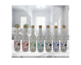 May include: Seven clear glass bottles with gold caps, each decorated with a hand-drawn design, a name, and the word "Coquito" in different colours. The bottles are displayed on a white surface, suggesting a festive theme.