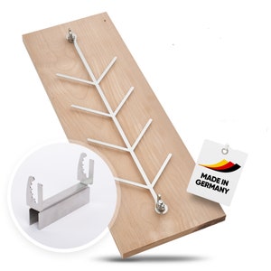 May include: A wooden wall-mounted coat rack with a silver metal tree-like design. The rack is attached to the wood with screws. A small, detailed inset shows a metal bracket. A tag reads "MADE IN GERMANY".