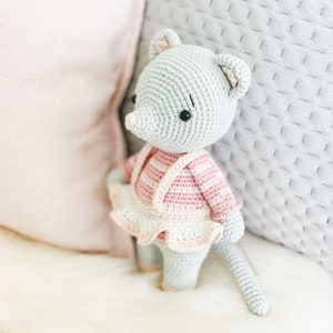 May include: A gray crocheted mouse wearing a pink and white striped shirt and a pink ruffled skirt. The mouse has black eyes and a long tail.