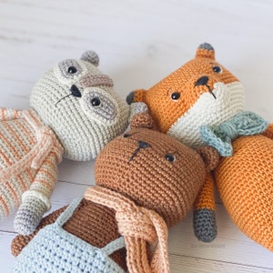 May include: A group of crocheted animal toys: an owl, a fox, and a bear. The owl is light grey, the fox is orange and white, and the bear is brown. Each toy has distinctive features and is crafted from soft yarn, perfect for children.