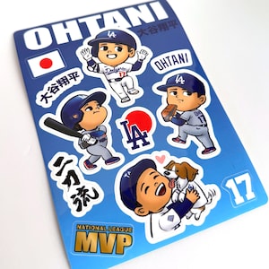 Może przedstawiać: Arkusz naklejek z kreskówkowymi ilustracjami baseballisty Ohtani w mundurze Dodgers. Arkusz zawiera tekst "OHTANI", "NATIONAL LEAGUE MVP" i numer "17". Tło jest niebieskie z japońską flagą.