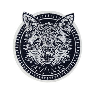 Può includere: Una toppa ricamata in bianco e nero con il viso di una volpe in un cerchio con un contorno bianco.