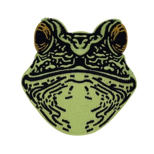 Op de afbeelding: Groene geborduurde kikkerpatch met zwarte contouren en bruine ogen. De kikker heeft zijn mond open en zijn tong is zichtbaar.
