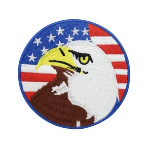 Pode incluir: Um remendo redondo bordado com a cabeça de uma águia careca olhando para a direita, com um bico e um olho amarelos. A águia está na frente de uma bandeira americana vermelha, branca e azul.