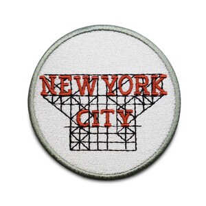 Könnte beinhalten: Ein weißer gestickter Aufnäher mit einem roten "NEW YORK CITY"-Design. Der Text ist von einem schwarzen Gittermuster umgeben.