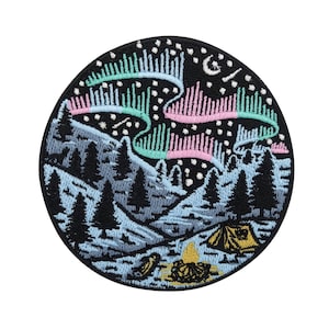 Peut inclure: Patch brodé représentant une scène de montagne bleu foncé avec une tente et un feu de camp sous une aurore boréale verte, rose et bleue vibrante.