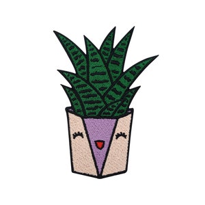 Può includere: Toppa ricamata di una pianta verde in vaso con un viso sorridente. Il vaso è rosa e bianco con un rivestimento interno viola.