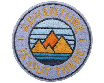 Puede incluir: Un parche bordado morado con el texto "Adventure is out there" en amarillo. El parche presenta una cordillera estilizada con una puesta de sol detrás.