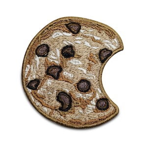 May include: A brown and tan embroidered patch shaped like a chocolate chip cookie with a bite taken out of it.
