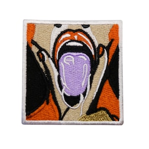 Op de afbeelding: Gestikte patch met een close-up van een open mond met een paarse tong die eruit steekt. De mond is omgeven door oranje, beige en zwart stof.