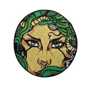 Könnte beinhalten: Gestickter Aufnäher mit dem Gesicht einer Frau, um deren Kopf sich grüne Schlangen winden. Die Frau hat einen Nasenring und ihre Augen sind schwarz umrandet. Der Hintergrund ist dunkelgrün.