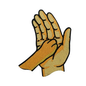 Op de afbeelding: Een geborduurde patch met twee handen, waarbij de ene de pols van de andere vasthoudt. De handen zijn geel met zwarte contouren. De patch is perfect om kleding, tassen of andere accessoires een vleugje speelsheid te geven.