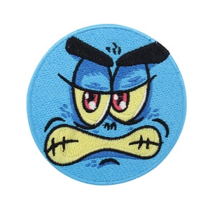 Puede incluir: Un parche bordado azul con una cara de dibujos animados. La cara tiene el ceño fruncido, ojos enojados y una boca fruncida.